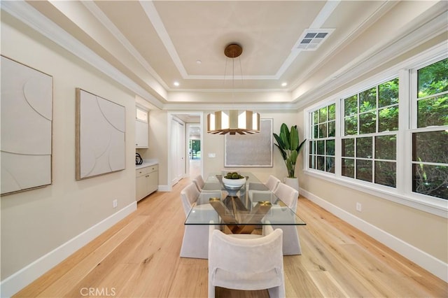 dining space featuring a raised ceiling, crown molding, and light wood-type flooring