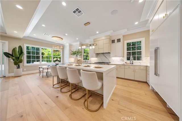 kitchen featuring light hardwood / wood-style flooring, pendant lighting, stainless steel gas stovetop, decorative backsplash, and a kitchen island