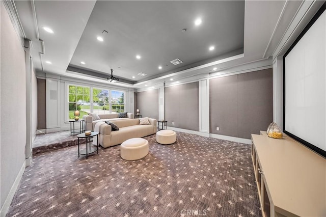 cinema room featuring ceiling fan, dark carpet, and a raised ceiling