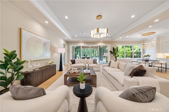 living room with light hardwood / wood-style floors, a raised ceiling, ornamental molding, and an inviting chandelier