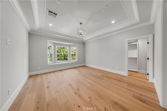 empty room featuring a raised ceiling, crown molding, light hardwood / wood-style floors, and an inviting chandelier