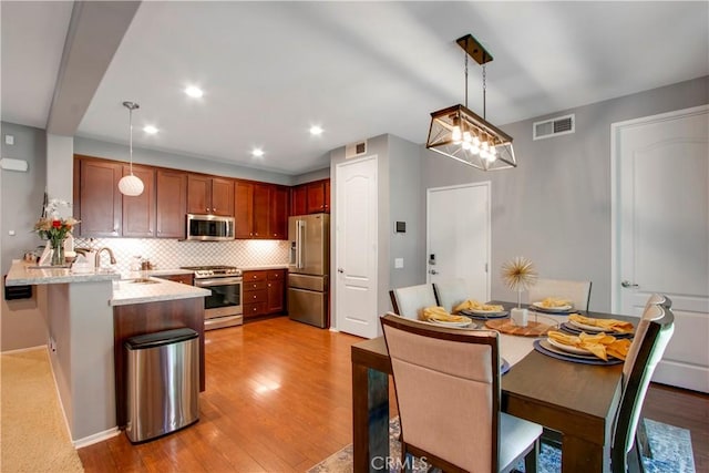 kitchen featuring kitchen peninsula, hanging light fixtures, stainless steel appliances, and light hardwood / wood-style flooring