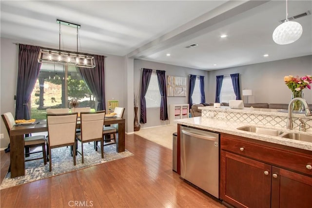 kitchen featuring light stone countertops, sink, stainless steel dishwasher, decorative light fixtures, and light wood-type flooring