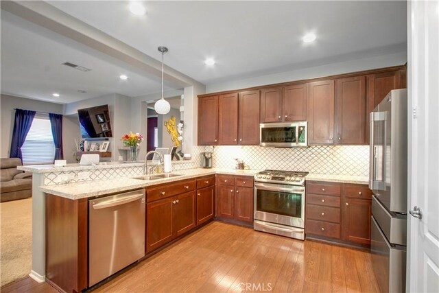 kitchen with sink, stainless steel appliances, kitchen peninsula, pendant lighting, and light wood-type flooring