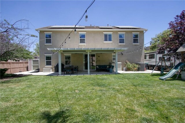 rear view of house with a lawn, solar panels, a playground, central AC unit, and a patio area