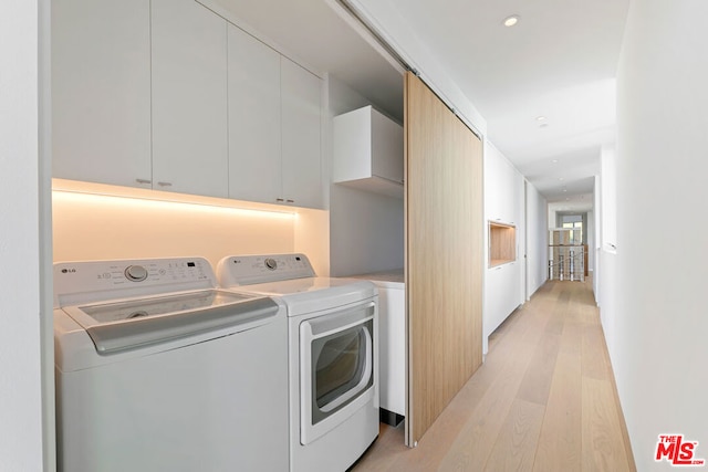 clothes washing area with cabinets, light wood-type flooring, and separate washer and dryer