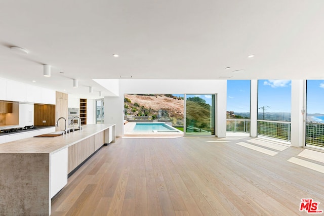 interior space featuring white cabinets, sink, a large island, light hardwood / wood-style floors, and gas cooktop