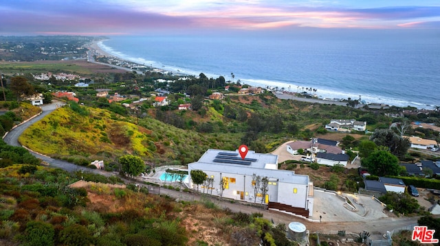 aerial view at dusk featuring a water view and a beach view