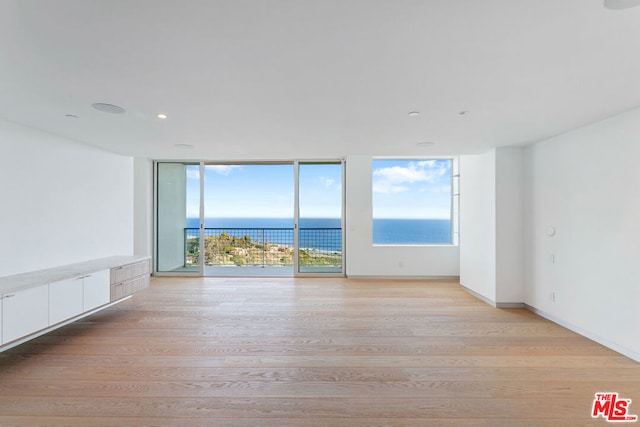 spare room with a water view, a wall of windows, and light hardwood / wood-style floors