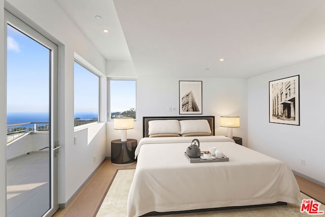 bedroom featuring light hardwood / wood-style floors, a water view, and access to outside