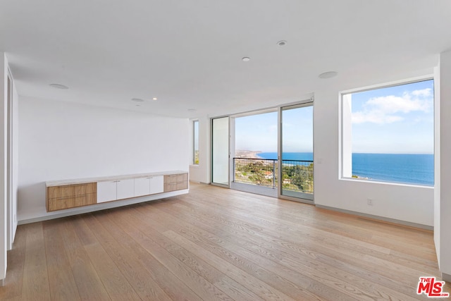 empty room featuring light hardwood / wood-style floors, a water view, a beach view, and a wealth of natural light