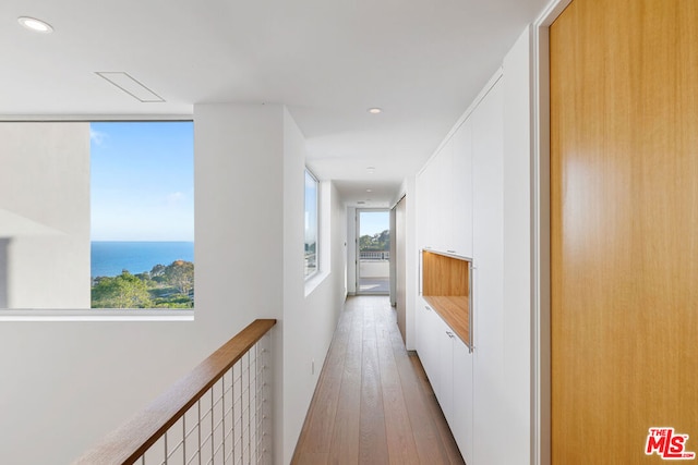 corridor with light hardwood / wood-style floors, a wealth of natural light, and a water view