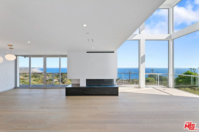 unfurnished living room featuring plenty of natural light, floor to ceiling windows, a water view, and light hardwood / wood-style flooring