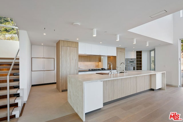 kitchen featuring white cabinetry, stainless steel double oven, tasteful backsplash, light hardwood / wood-style flooring, and an island with sink