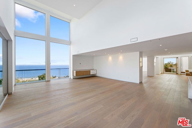 unfurnished living room featuring a towering ceiling, a water view, and light hardwood / wood-style floors