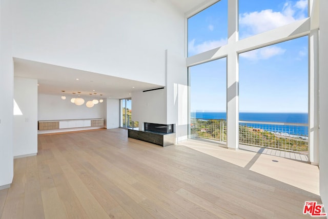 unfurnished living room with a water view, a high ceiling, and light hardwood / wood-style flooring