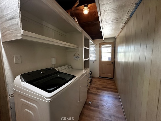 clothes washing area with washer and clothes dryer, dark hardwood / wood-style floors, and wood walls