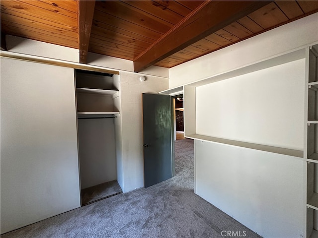 unfurnished bedroom with dark colored carpet, beam ceiling, a closet, and wood ceiling