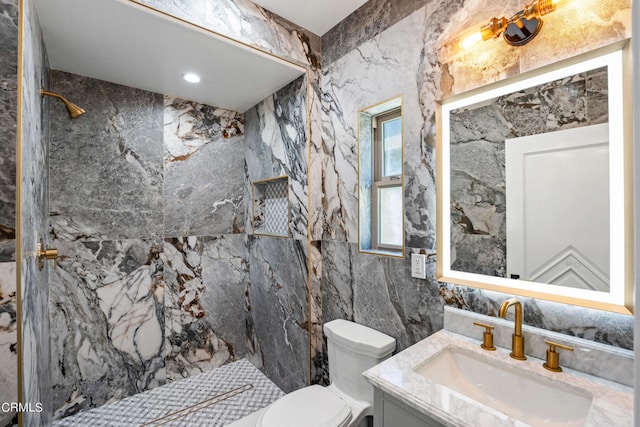 bathroom featuring a tile shower, vanity, tile walls, and toilet