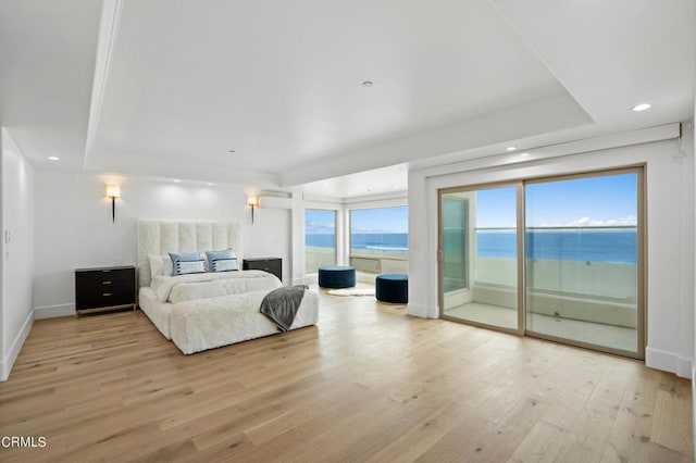 bedroom with multiple windows, access to outside, a water view, and light wood-type flooring