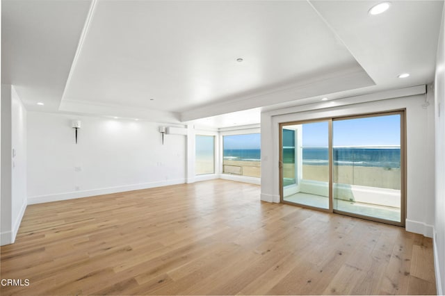 spare room featuring light hardwood / wood-style flooring, a tray ceiling, and a water view