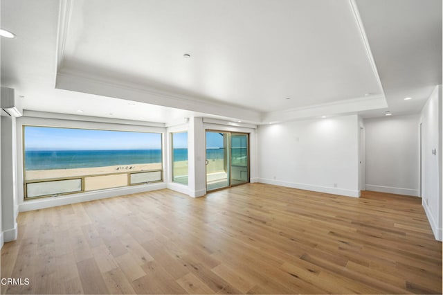 unfurnished living room with a water view, a tray ceiling, and light hardwood / wood-style flooring