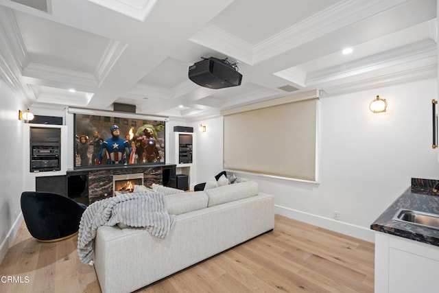 home theater featuring crown molding, a stone fireplace, coffered ceiling, and light hardwood / wood-style flooring