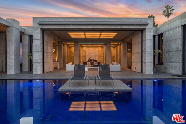 pool at dusk featuring a tile fireplace and a patio area