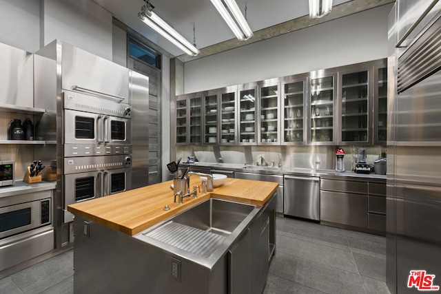 kitchen featuring stainless steel appliances, a center island with sink, stainless steel counters, and sink