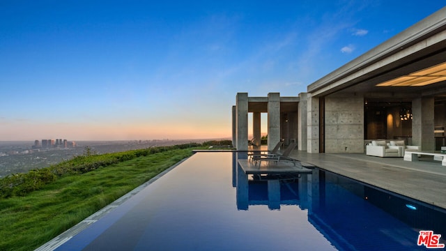 pool at dusk featuring an outdoor hangout area and a patio