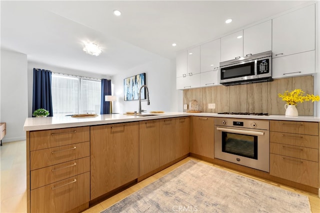 kitchen with white cabinetry, sink, kitchen peninsula, decorative backsplash, and appliances with stainless steel finishes