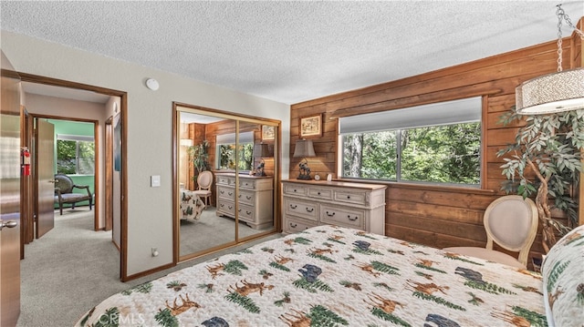 carpeted bedroom featuring a textured ceiling, wood walls, and a closet