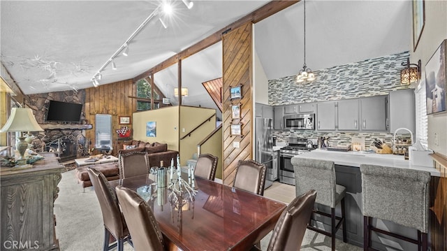 dining area featuring light colored carpet, wooden walls, a fireplace, and high vaulted ceiling