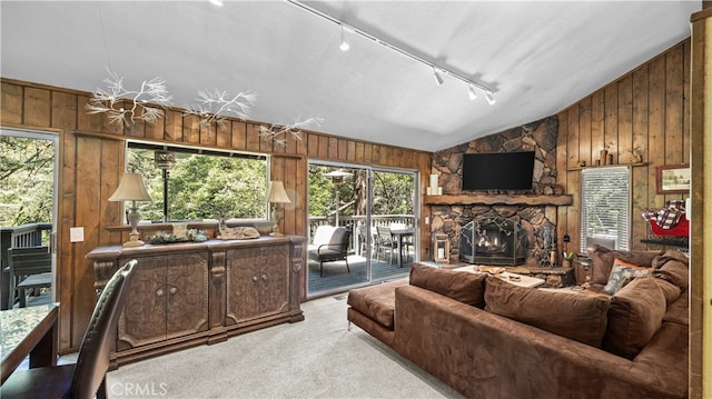 living room with track lighting, wood walls, lofted ceiling, light carpet, and a stone fireplace