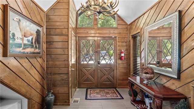 entryway with lofted ceiling, wooden walls, a chandelier, and french doors