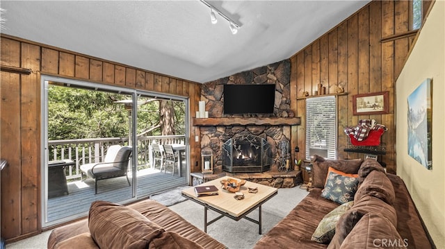 carpeted living room featuring a healthy amount of sunlight, wood walls, a stone fireplace, and vaulted ceiling