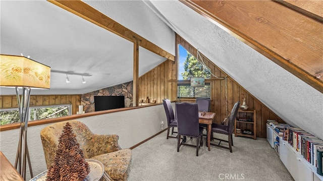 carpeted dining room with a textured ceiling, wooden walls, vaulted ceiling, and rail lighting