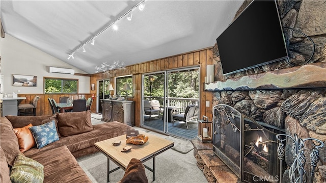 living room with a stone fireplace, lofted ceiling, track lighting, wooden walls, and a wall mounted AC