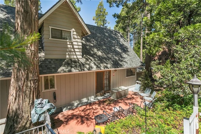 view of side of home with a patio and a shingled roof