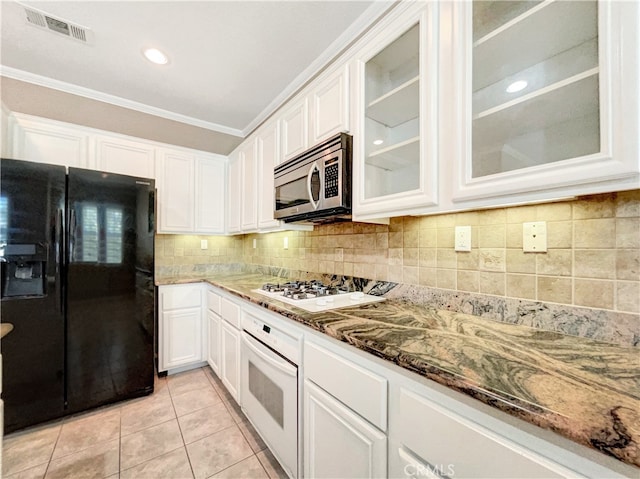 kitchen featuring white cabinetry, dark stone counters, ornamental molding, light tile patterned flooring, and white appliances