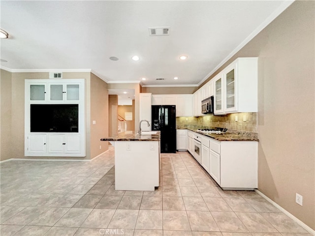 kitchen with a center island with sink, white cabinets, stainless steel appliances, and dark stone counters