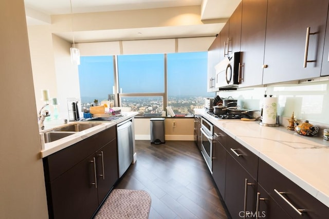 kitchen with hanging light fixtures, a sink, stainless steel appliances, light stone countertops, and dark wood-type flooring