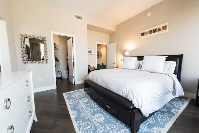 bedroom featuring a walk in closet, dark wood finished floors, visible vents, and baseboards