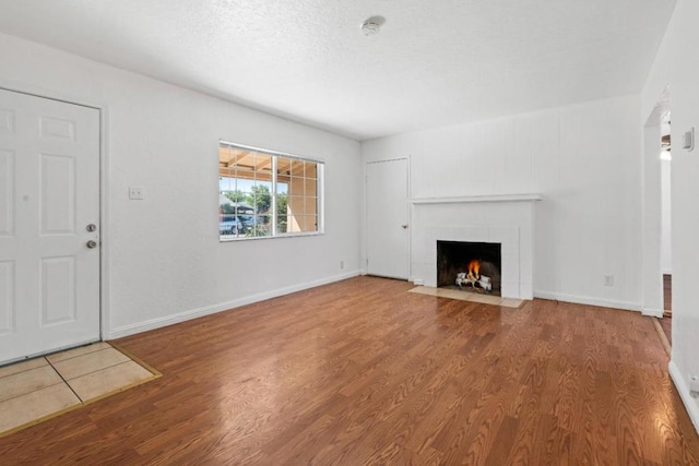 unfurnished living room featuring a brick fireplace, a textured ceiling, and hardwood / wood-style flooring