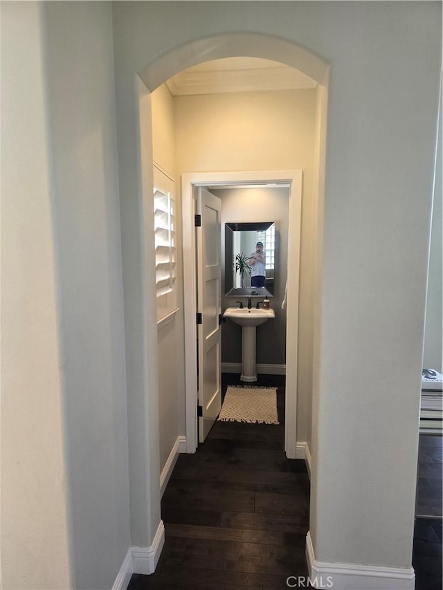 hallway featuring baseboards, arched walkways, and dark wood finished floors