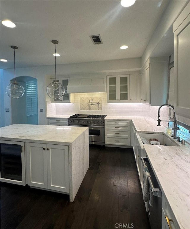 kitchen featuring high end stove, visible vents, white cabinets, light stone countertops, and pendant lighting