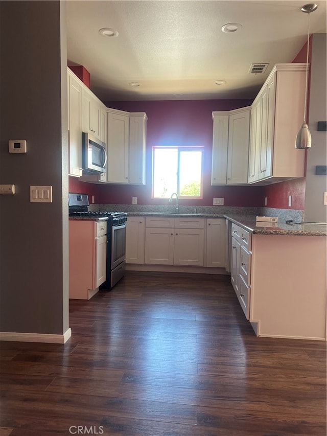 kitchen with appliances with stainless steel finishes, dark wood-type flooring, white cabinetry, and hanging light fixtures