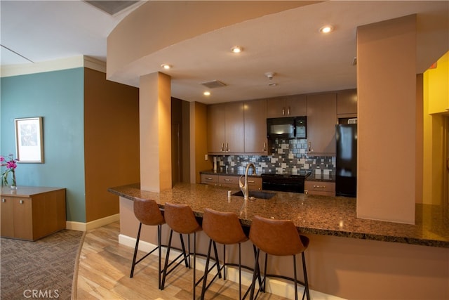 kitchen featuring kitchen peninsula, sink, black appliances, a kitchen bar, and light hardwood / wood-style floors