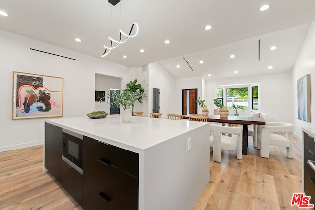 kitchen with vaulted ceiling, black microwave, decorative light fixtures, light hardwood / wood-style floors, and a large island