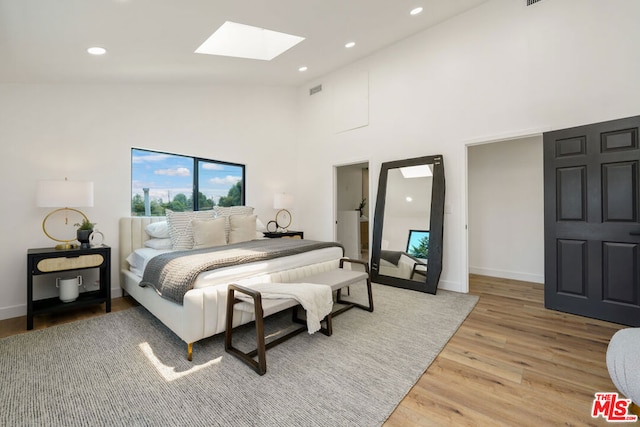 bedroom featuring a skylight, high vaulted ceiling, and wood-type flooring